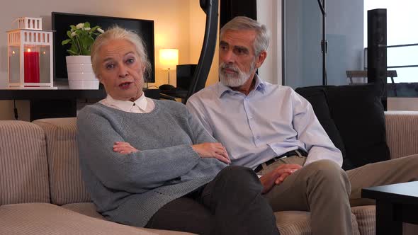 An Elderly Couple Sits on A Couch in An Apartment and Talks to The Camera