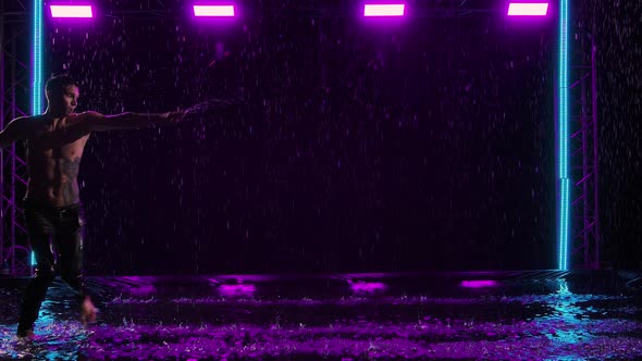 Wet Male Ballet Dancer Performs Pirouette Among Raindrops Performing in Dark Studio on Water Surface