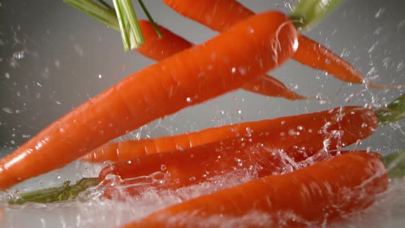 Carrots falling on water surface. Slow Motion.