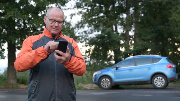 Happy Senior Man Using Phone On The Side Of The Road