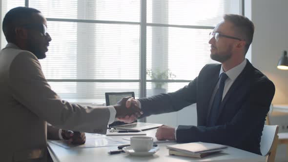 Two Multiethnic Businessmen Shaking Hands and Speaking in Office