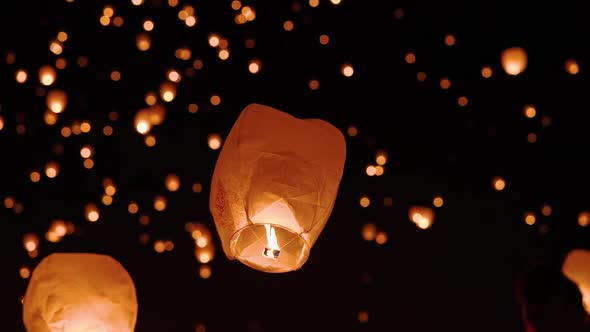 Young woman letting go of sky lantern into the sky full of others glowing