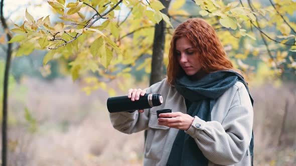 Beautiful Redhaired Woman Drinks Tea From Thermos in the Autumnal Forest