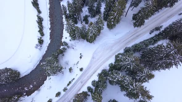 Aerial drone view of a road, river, trees and a forest in the snow covered mountains