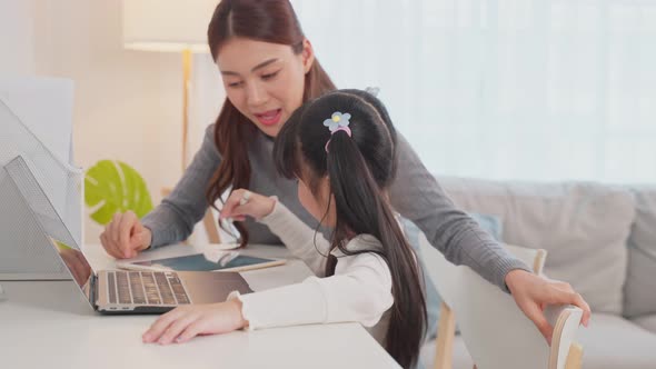 Asian little young girl kid learning online class at home with mother's support in living room.