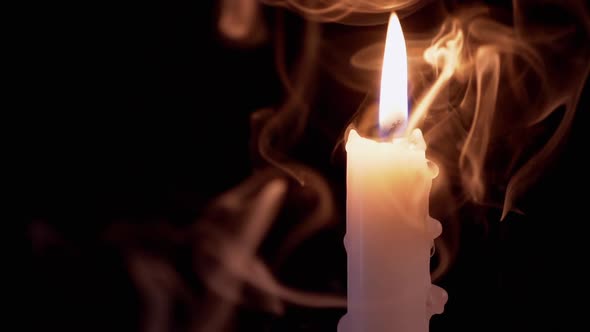 Candle with Dripping Wax Burns in a Cloud of Smoke on Black Background