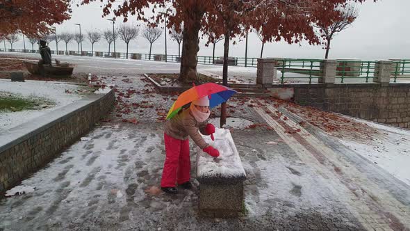 Child girl with colorful umbrella plays outdoor kicking snowball. Slow-motion