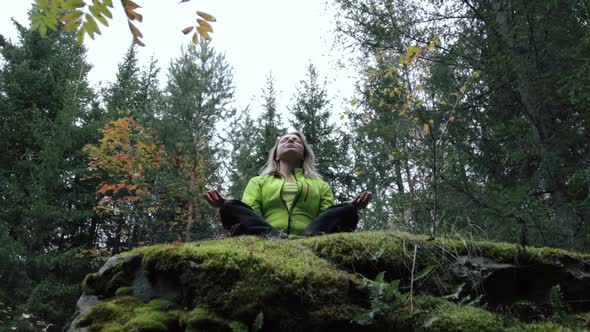 Woman meditating on a rock in the forest