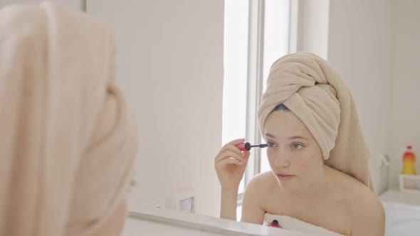 Teenage girl applying makeup in front of the bathroom mirror