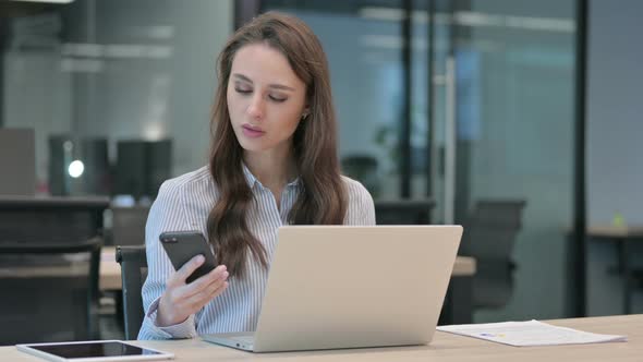 Young Businesswoman Working on Smartphone and Laptop in Office