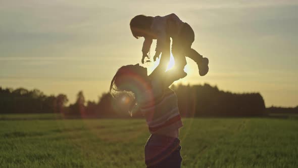 Happy Young Mother Throws Her Baby Daughter in Her Arms at Sunset