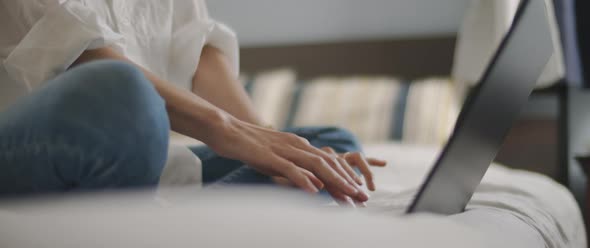 Woman hands typing something on a laptop keyboard in the bedroom.