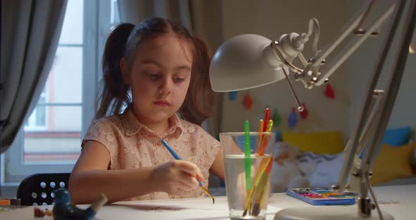 Preschool Girl Paints with Watercolor Paints at Home at the Table