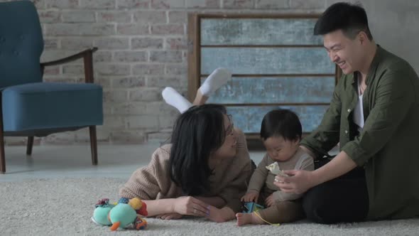 Happy Young cheerful Asian family inside in room on floor playing with small son