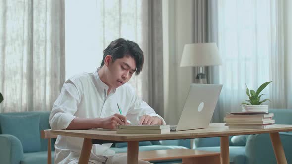 Asian Man Student Look At Computer Screen And Write In The Notebook While Studying At Home