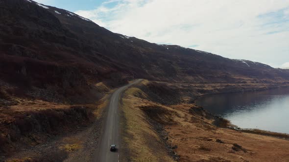 Drone Tracking Car Driving By Fjord And Towards Mountains