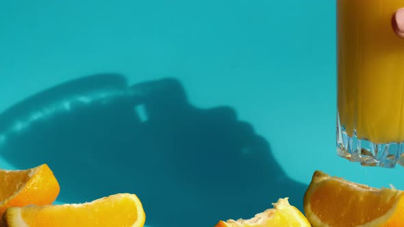 Female Hand Put and Take Glass of Fresh Squeezing Orange Juice with Sliced Fruits on Blue Background