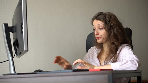 Young Female Office Manager in White Shirt and Curly Hair is Sitting at the Table and Typing Using