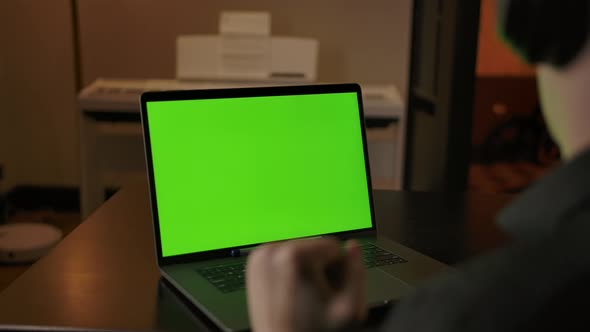 Caucasian Male in Headphones Listening Music Behind Green Screen Laptop