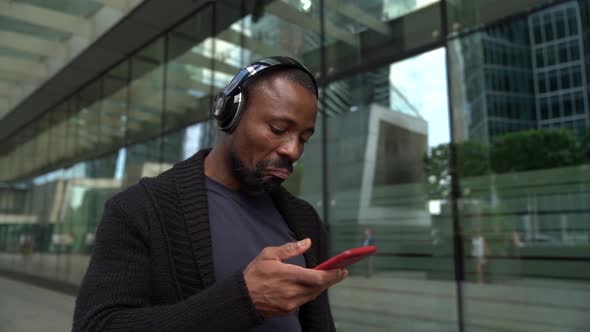 Portrait of an African Man in Dark Clothes, Wearing Headphones and a Beard. He Stands with a