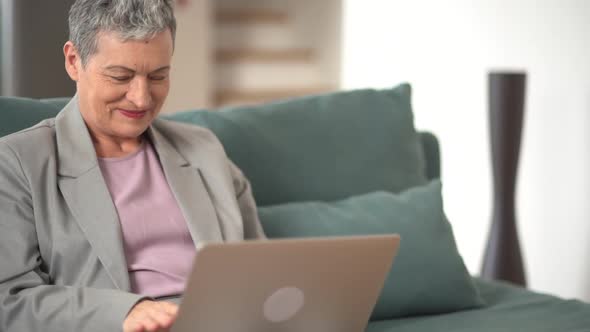 Mature Woman in a Gray Suit and with Short Gray Hair is Having a Video Call Using a Laptop and