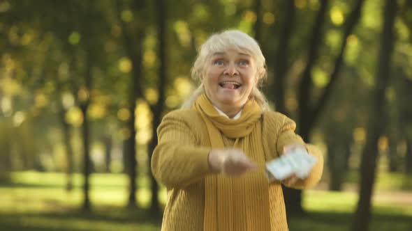 Happy Senior Old Lady Throwing Stack of Dollar Bills in Park, Planned Retirement