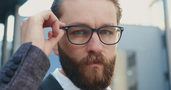 Office Manager which Correcting His Glasses while Looking at Camera Outdoors Near Office Building 