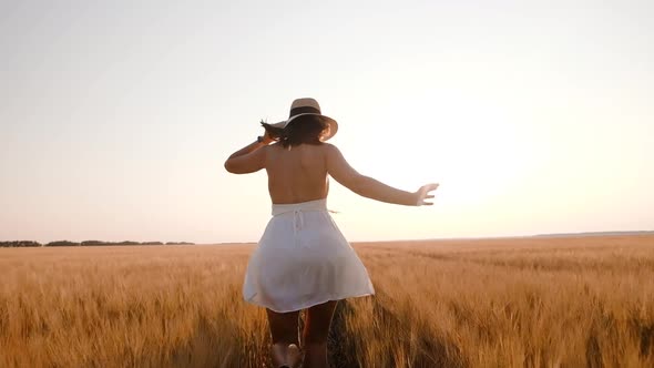 Happy Free Young Woman Runs in Slow Motion Across Field Touching Ears of Wheat with Her Hand