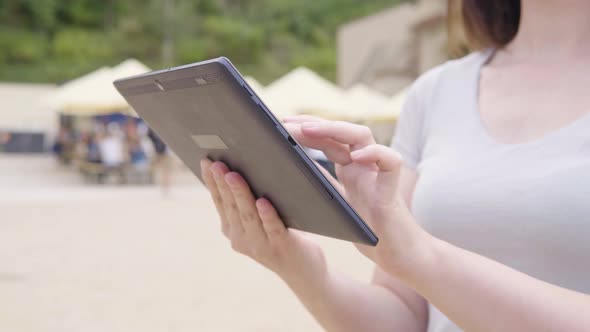 A Caucasian Woman Works on a Tablet in a City Park  Closeup on the Hands and the Phone