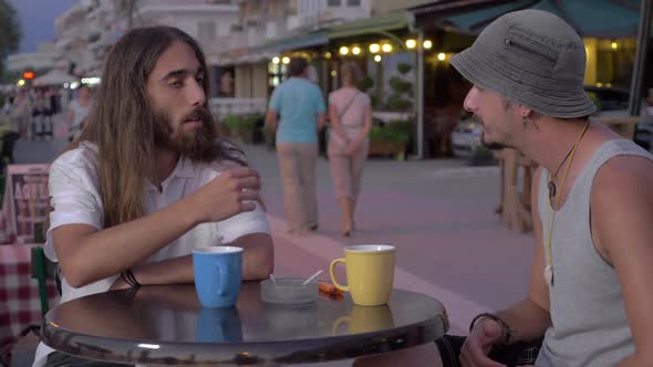 Two Men Having Talk and Drinks in Street Cafe