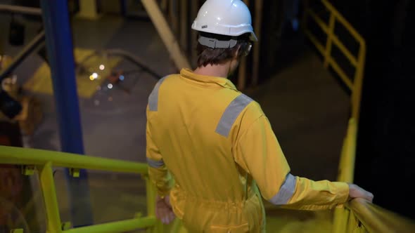 Young Man in a Yellow Work Uniform, Glasses and Helmet in Industrial Environment,oil Platform or