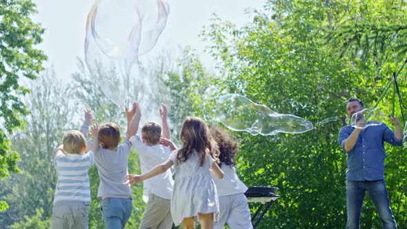 Children Enjoying Catching Giant Bubbles During Outdoor Performance