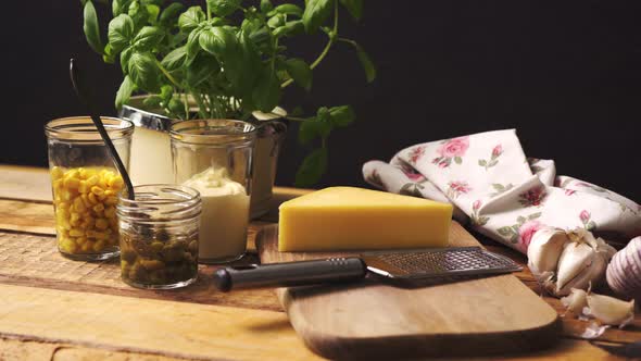 Cheese on Chopping Board and Grater with Fresh Basil on Wooden Kitchen Table