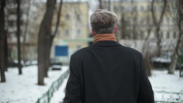 Back view of the leaving gray-haired man in a coat. A man walks through the park