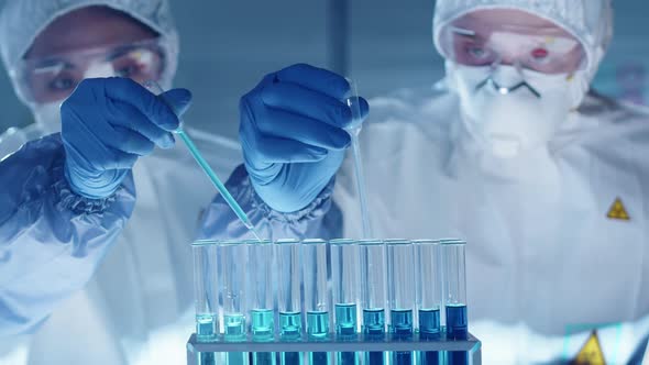 Two Lab Scientists Dripping Blue Liquid into Test Tubes