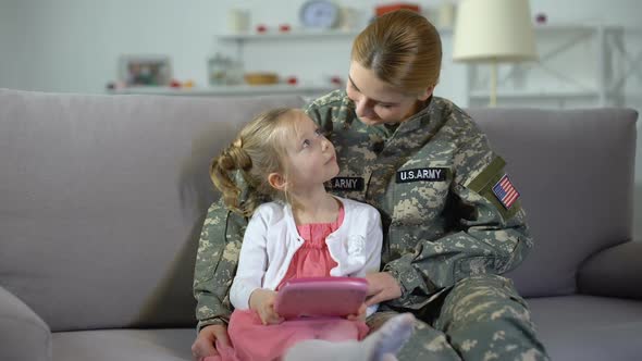 Mother in US Army Uniform and Little Daughter Playing Game on Tablet Together