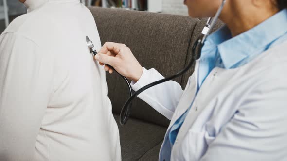 Woman Doctor Examining Patient By Phonendoscope While She is Making Some Deep Breaths Sitting on