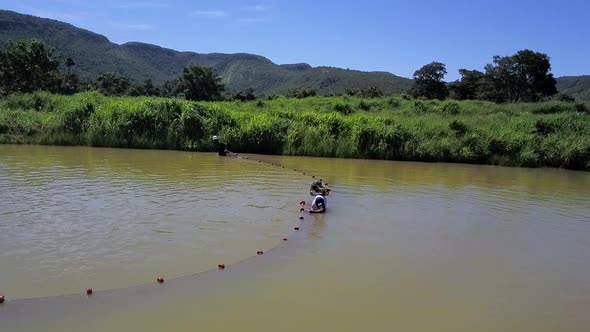 Three fishermen in a small pond use a large net to corner and catch fish on a fish farm in rural Bra