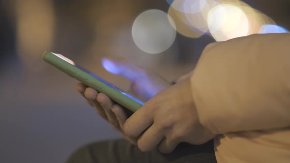 Closeup of female hands holding mobile phone browsing internet on city street with blurred