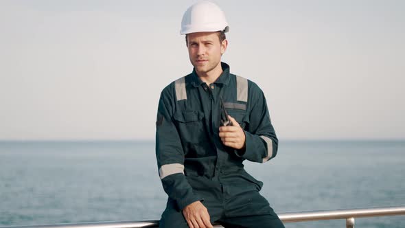 Young Port Worker in Helmet and Coverall Using Vhf Radio Controlling Work Process in Shipping Port