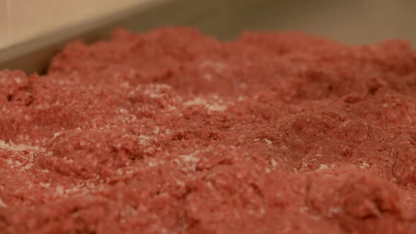 Salt falling onto raw beef mince in preparation for handmade burger production close up slow motion