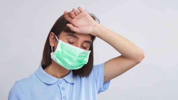 Woman in Respiratory Mask Measures Her Temperatury with Arm Touching Forehead
