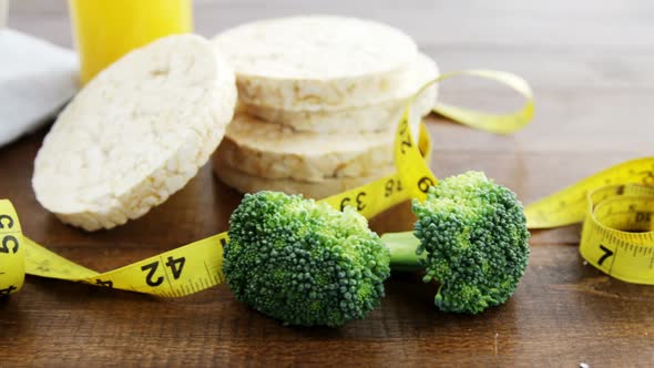 Broccoli, granola bar, yellow cherries and measurement tape on wooden table