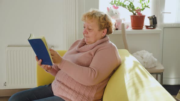 Old Fat Woman Relaxing on Comfortable Sofa Reading Paper Book at Home