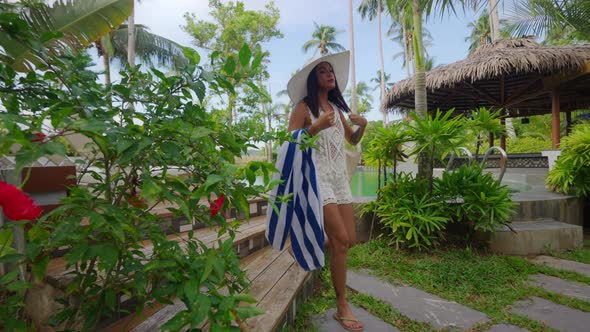 Woman In Sun Hat Walking With Beach Towel On Resort Path