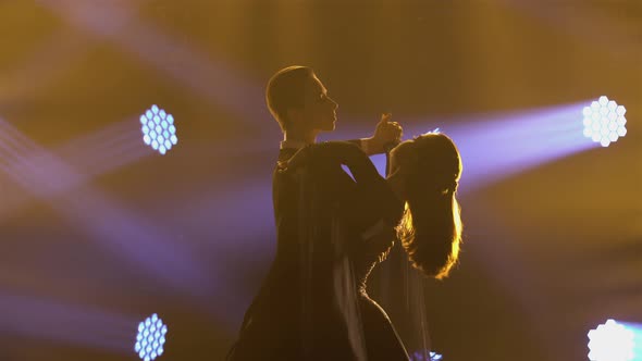 Professional Couple of Ballroom Dancers Waltzes on an Iparket in Dark Studio Against Backdrop of