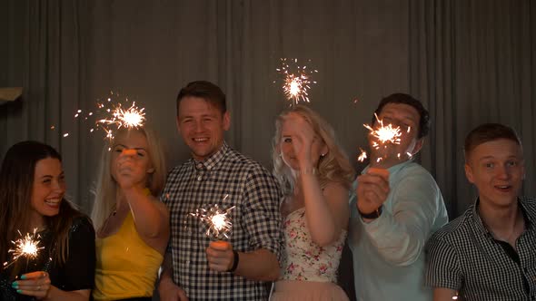 Group of Cheerful Young People Carrying Sparklers.