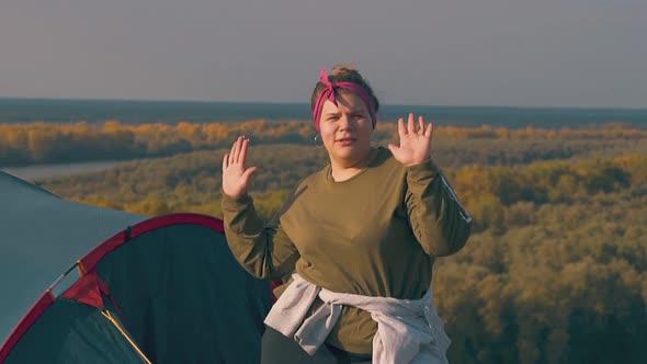 Joyful Plump Girl Dances with Raised Hands Near Blue Tent