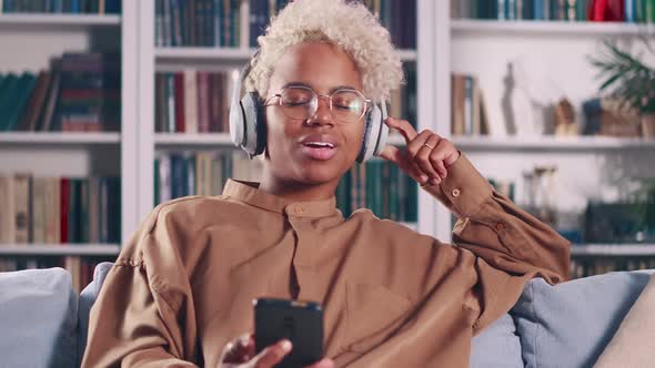 Young African American Woman Listen to Music in Wireless Headphones Sits at Home