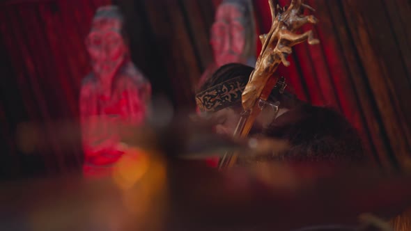 Musician Plays Instrument with Tree Root on Head in Cabin